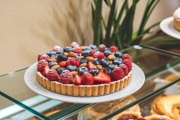 Freshly Baked Fruit Tart with Golden Crust, Berries, Almonds, and Powdered Sugar on Display in a Cozy Bakery Setting