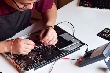 Computer technician wearing glasses A laptop motherboard repairman is using an IC meter to find...