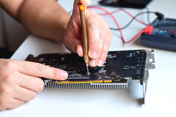 computer technician laptop motherboard repair technician A technician is using a screwdriver to take apart a motherboard for repair on his workbench.	