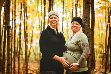 Lesbian couple having fun on autumn forest with future newborn child on woman belly.