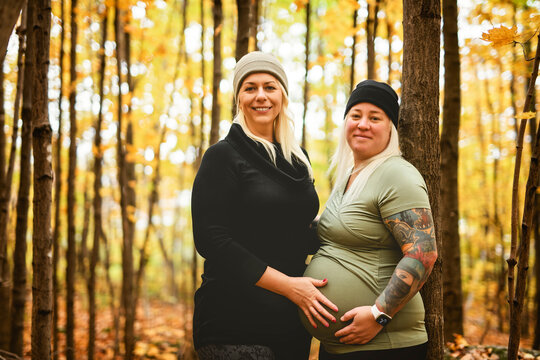 Lesbian couple having fun on autumn forest with future newborn child on woman belly.