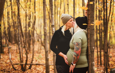 Lesbian couple having fun on autumn forest with future newborn child on woman belly.