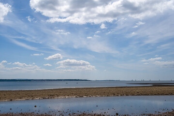 beautiful beach at Hill Head Hampshire England with clouds and blue sky reflecting in the the water and The Isle of Wight in the background