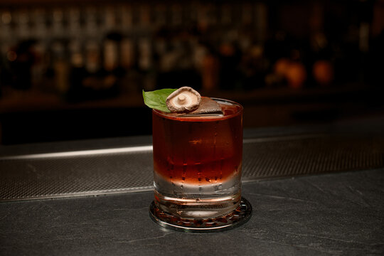 Glass of cocktail with an ice, on which lies a green leaf and a mushroom cap
