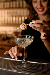 Cute smiling female bartender holding skewer with banana and fried sugar on it over glass