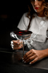 Focus on a glass with a brown cocktail and an ice cube in it, surrounded by smoke