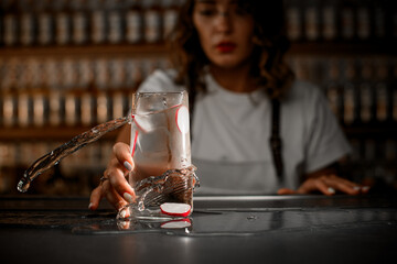 Female bartender shakes a glass with a transparent iced cocktail in which radish rings float