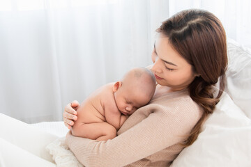 Asian loving mother caring for her newborn baby at home, sleeping baby in her arm with love and care, adorable cuddle sleep on chest mom and safe, healthcare infant and mother nurturing concept