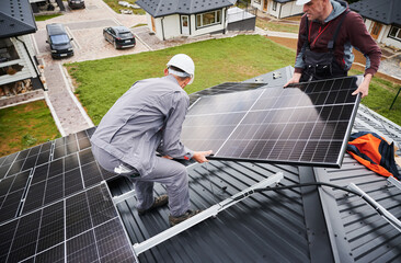 Technicians installing solar panel system on roof of house. Men workers in helmets carrying...