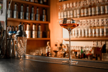 Tall glass stands on the bar counter, half filled with a cocktail with a huge ice cube
