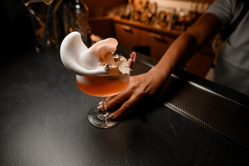 Female bartender's hand shakes a glass with foamy cocktail, spinning it in a circle