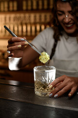 Female barman, laughing merrily, lowers a piece of marmalade with shaped tweezers into a glass