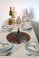 Table set for Christmas meal with plates, glasses, holiday decorations, lit candles and wine. Selective focus.