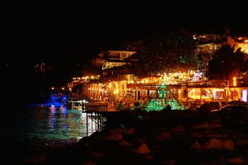 Naklejka premium view of the illuminated city by the sea. Restaurants and cafes on the sea beach at night