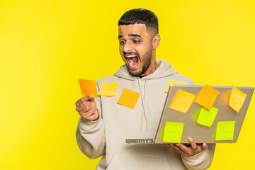 Exhausted freelancer Indian man with pasted sticker notes use laptop computer having concentration problem creative crisis. Nervous Arabian guy confused by big routine work loading yellow background