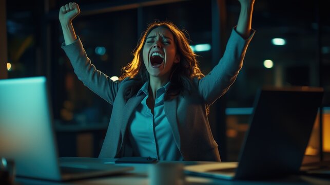 A woman expresses joy and excitement after reaching a major milestone in her career while working late at night in a contemporary office setting