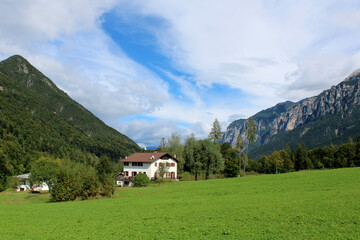Vallata con prato case bosco montagne e cielo con nubi  in Val di Sella