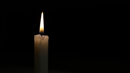 Single white candle burns in darkness, with a gently flickering flame casting a warm glow. The soft light creates a serene atmosphere, evoking feelings of hope and tranquility