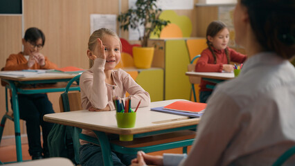 Unrecognizable woman teacher tutor ask children lesson check knowledge of pupils schoolboy little African American boy raise hand answer clever smart child kid son reading in book at class school