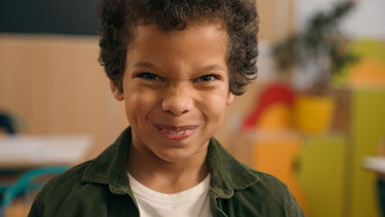 Portrait little African American boy looking at camera primary school adorable biracial guy kid schoolboy son child baby pupil student in kindergarten studying education smile laughing grimacing face