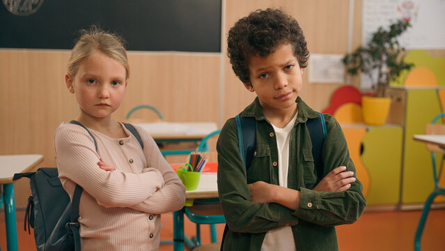 Serious offended confident African and Caucasian little school children multiracial diverse girl and boy kids pupils schoolchildren together class study primary education posing hands crossed offense