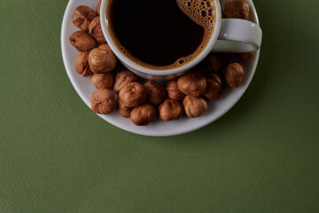 Enjoying a warm cup of coffee accompanied by roasted hazelnuts on a green background. top view