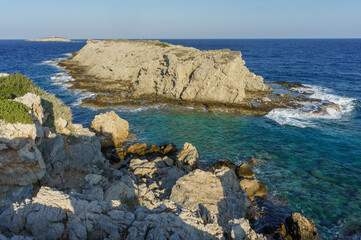 Vibrant coastal landscape with rocky shores and clear blue waters at sunset in a secluded location.