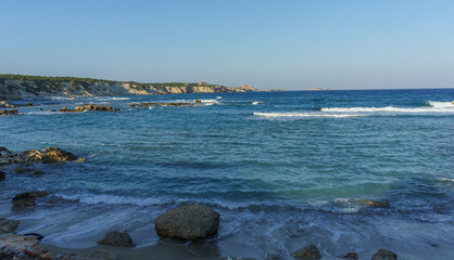 Tranquil coastal view at sunset, waves gently lapping against rocky shore near serene cliffs.