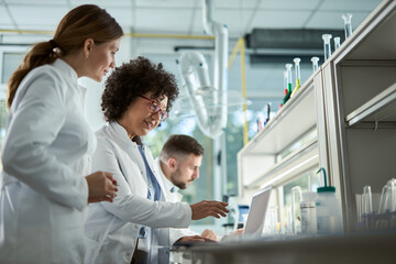 Team of biotechnologists cooperating while reading scientific data on a computer in laboratory.