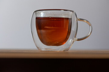 Warm embrace of tea in a clear glass cup resting on a wooden table during a peaceful afternoon