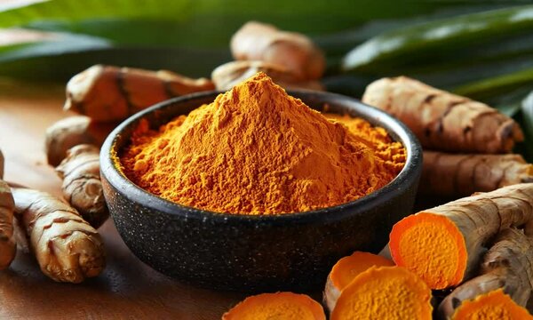 Turmeric powder in a wooden bowl surrounded by turmeric roots