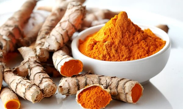 Turmeric powder in a white bowl with turmeric roots on a white background