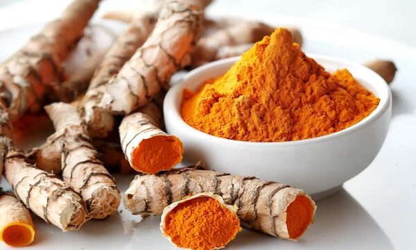 Turmeric powder in a white bowl with turmeric roots on a white background