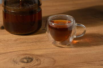 A warm cup of tea resting on a wooden table alongside a stylish glass teapot in a cozy setting