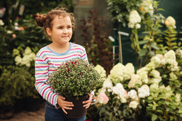 Little cute girl kid buying flowers. Choosing plants in a local garden center.