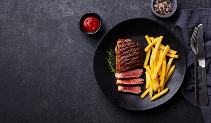 Beef Steak medium rare with French fries on a black plate. Dark background. Copy space. Top view.