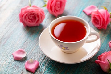 Cup of tea with pink rose. Colorful turquoise wooden background. Close up.