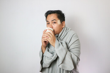 Adult Asian man wearing blanket and holding warm drink when got flu