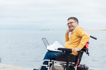 Man Sitting in Wheelchair Working on Laptop Talking on Smartphone