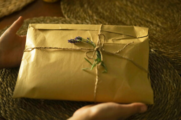 Female hands holding a gift box made from eco paper decorated with lavender sprigs. 