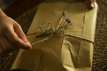 Hand opens a gift box made from eco paper decorated with lavender sprigs. 