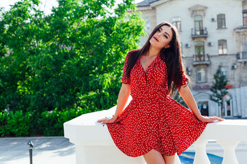 Beautiful brunette woman in a red summer dress walking through the streets of the city