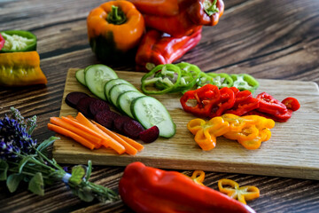 Slicing colorful sweet bell peppers, cucumbers, carrots and other vegetables, preparing a dish