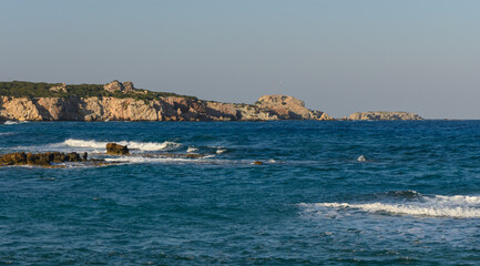 Waves gently lapping against the rocky coastline under a serene sky at golden hour.