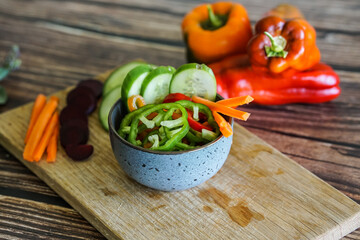 Slicing colorful sweet bell peppers, cucumbers, carrots and other vegetables, preparing a dish