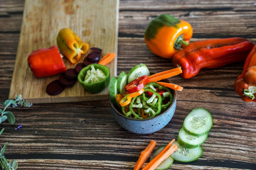 Slicing colorful sweet bell peppers, cucumbers, carrots and other vegetables, preparing a dish