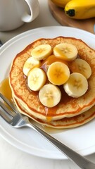 A plate of banana pancakes topped with slices of banana and honey, set on a cozy breakfast table.