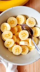 Sliced bananas arranged in a bowl, ready for breakfast or a healthy snack, with a spoon beside the bowl