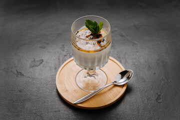 Elegant panna cotta dessert with passion fruit topping and mint in a glass on a wooden coaster