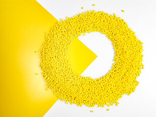 Yellow masterbatch granules form a circular frame on a white and yellow background, a polymer that...